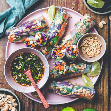 Vietnamese Sommerrollen liegen auf einem Tisch neben Dip-Sauce, Erdnüssen und Limetten.