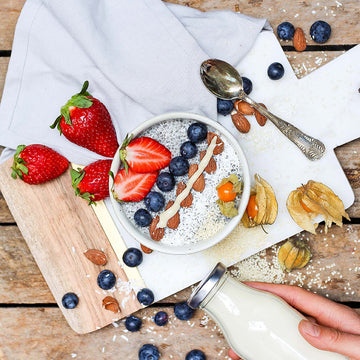 Eine Schüssel mit Chia-Pudding, dekoriert mit Früchten und Nüssen, neben Milchflasche.