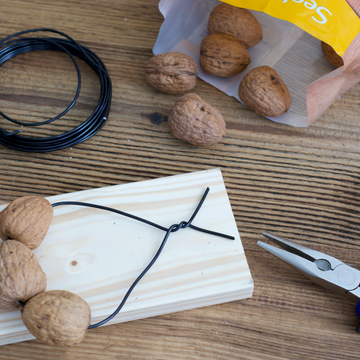 Walnüsse liegen auf Holzbrett, Draht fädelt sie auf, Zange und Verpackung daneben.