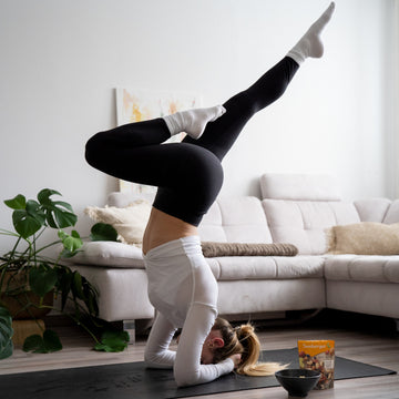 Eine Person macht einen Kopfstand auf Matte im Wohnzimmer neben Sofa.