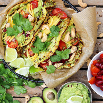 Tacos gefüllt mit Gemüse und Guacamole, dekoriert mit Limetten und Koriander auf Holztisch.