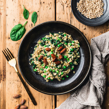 Risotto auf Teller, garniert mit Mandeln und Erbsen, auf Holztisch serviert.